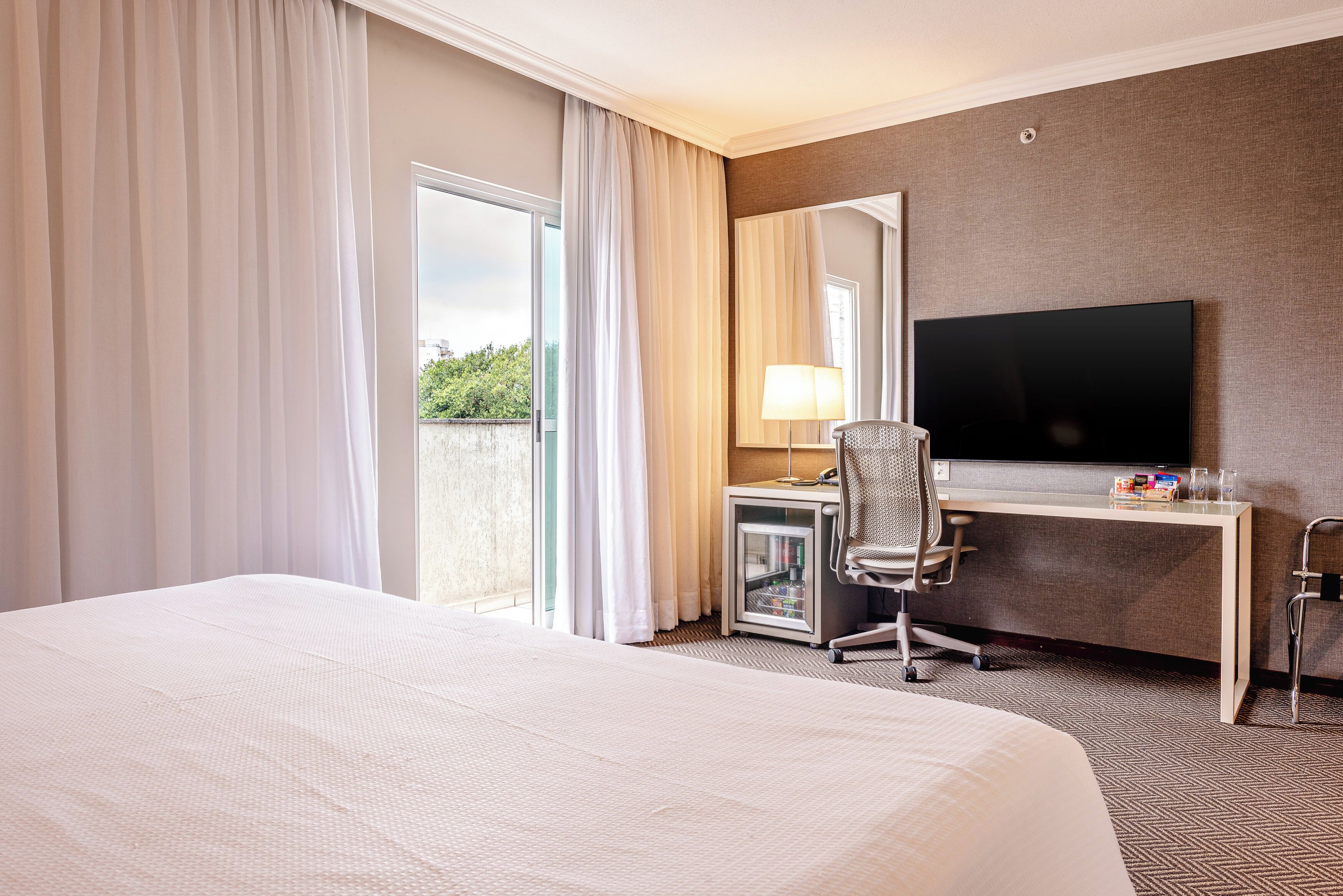 Een hotelkamer met een groot bed, een bureau met computer, een televisie en een raam met gordijnen.