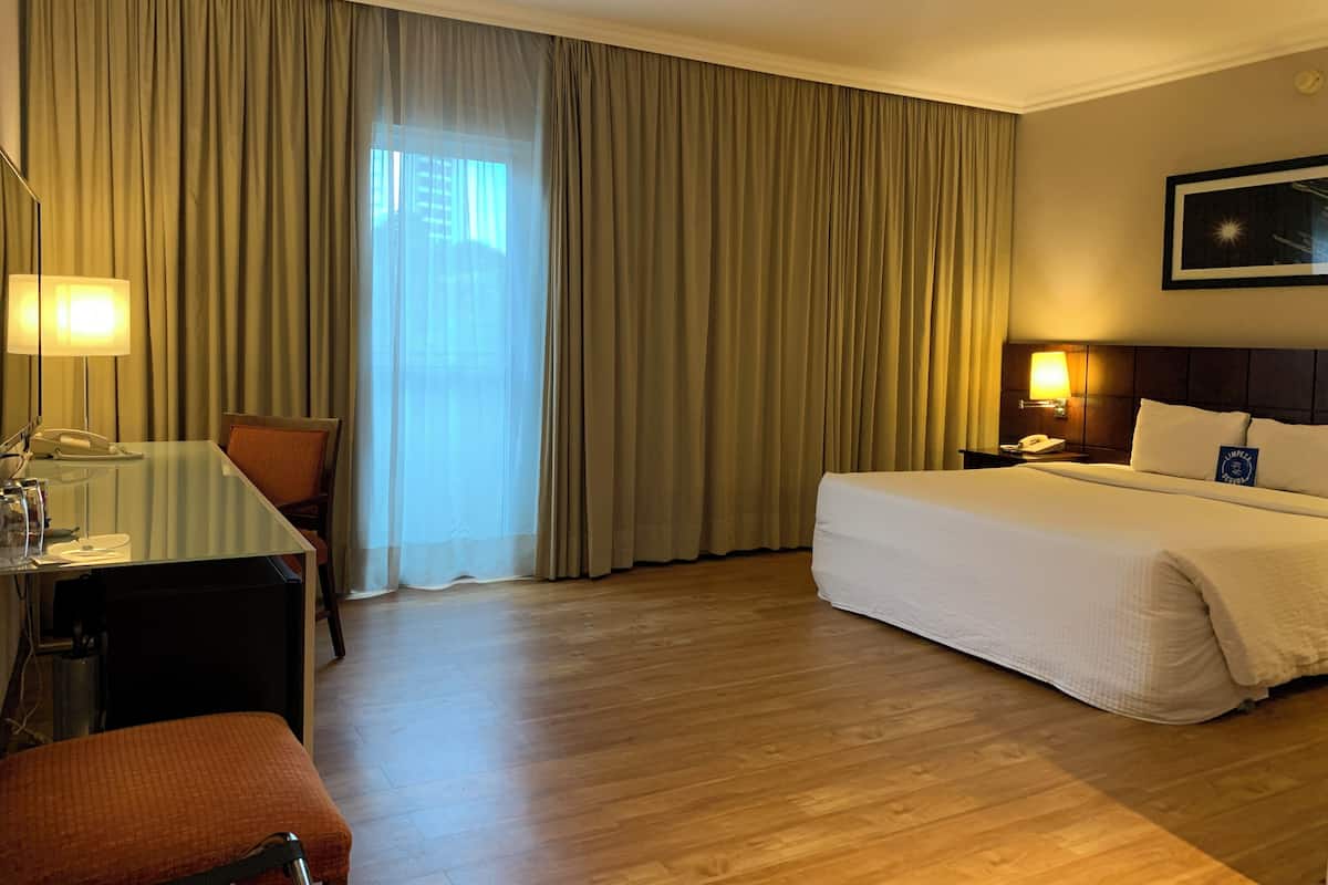 Une chambre d’hôtel équipée d’un lit, d’un bureau, d’une chaise, d’un téléphone et d’une fenêtre avec des rideaux.