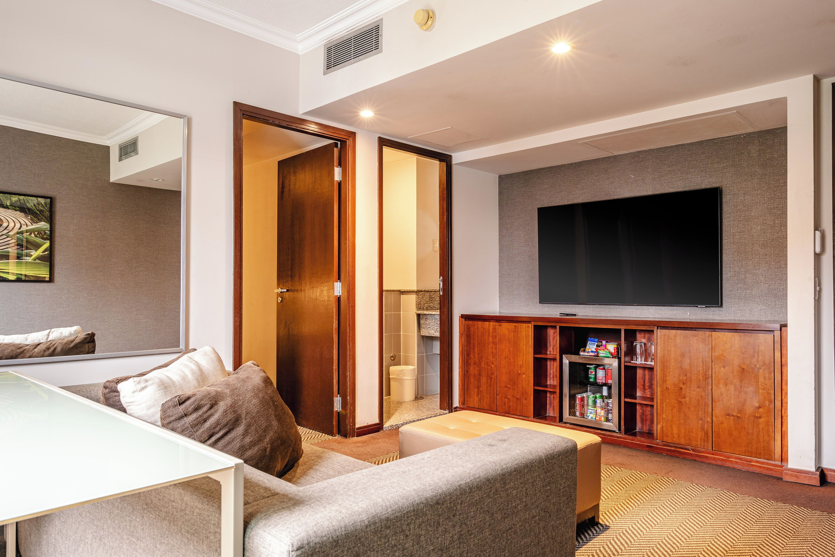 A modern living room with a sofa, a coffee table, a flat-screen TV mounted on the wall, and a wooden entertainment unit.