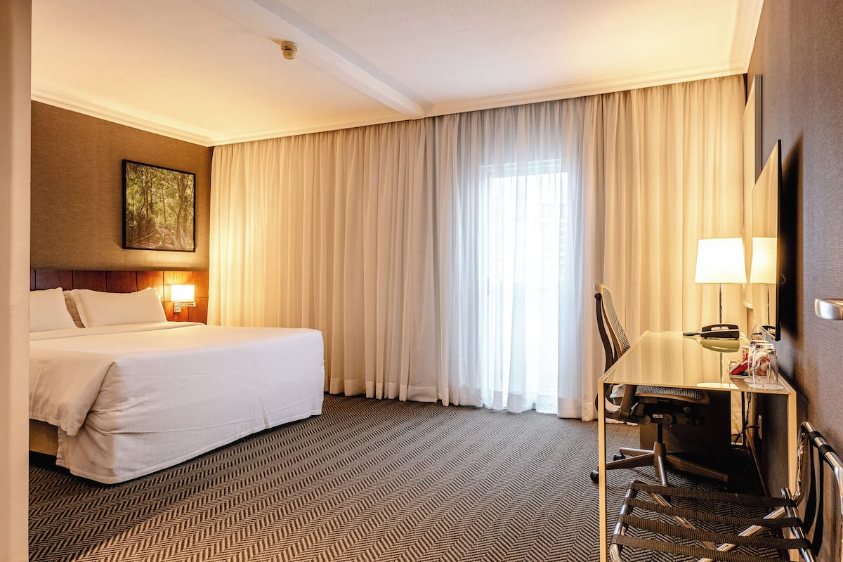 Une chambre d’hôtel avec un grand lit, un bureau avec une chaise, une lampe et un tableau au mur.