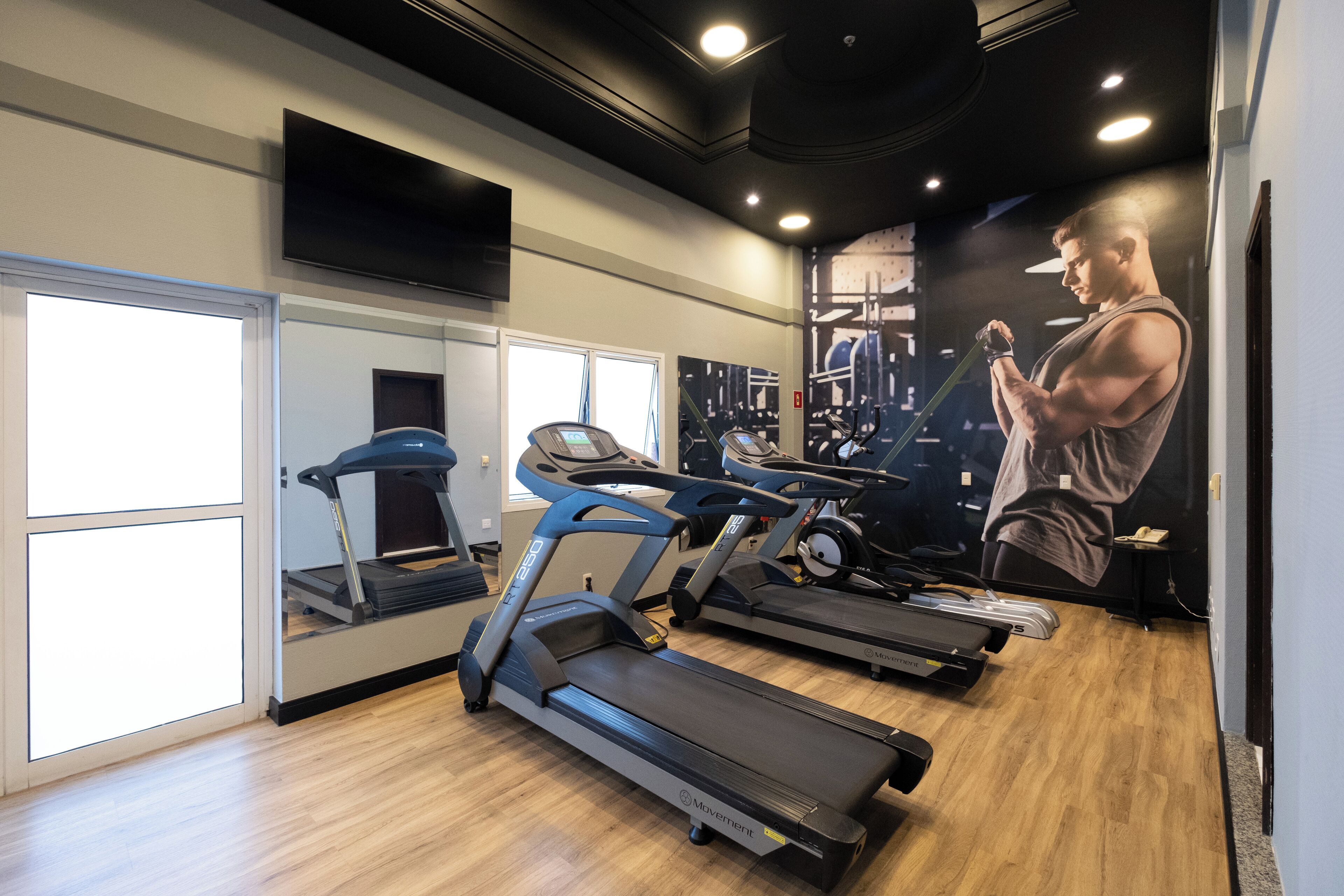 A gym with treadmills, a mirrored wall, and a large poster of a muscular man lifting weights.