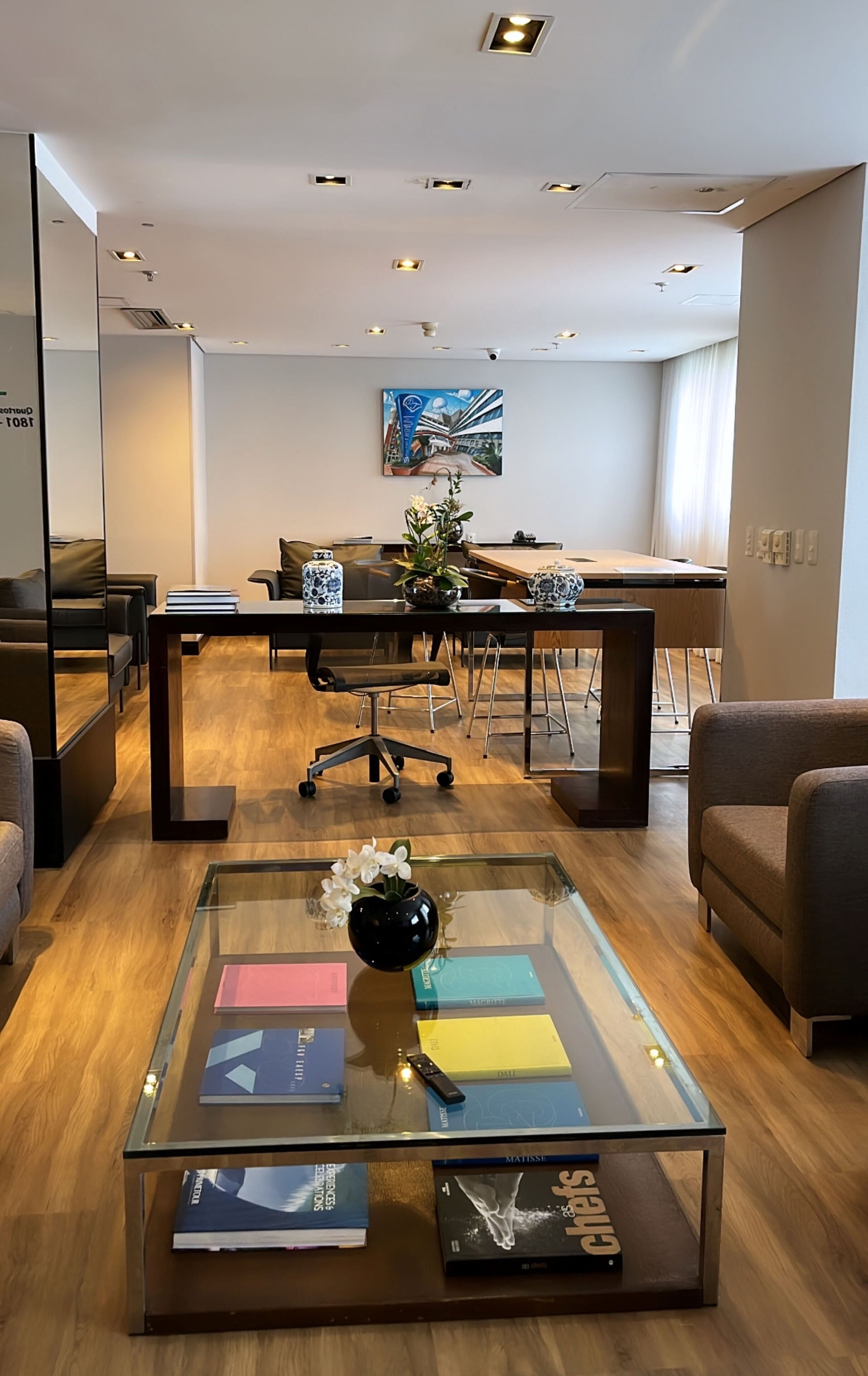 Un espacio de oficina moderno con una mesa de centro de vidrio, sofás de cuero y una zona de comedor con un cuadro grande en la pared.