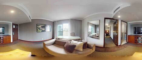Una habitación de hotel moderna con un sofá curvo, una mesa de comedor, un televisor y un espejo grande.