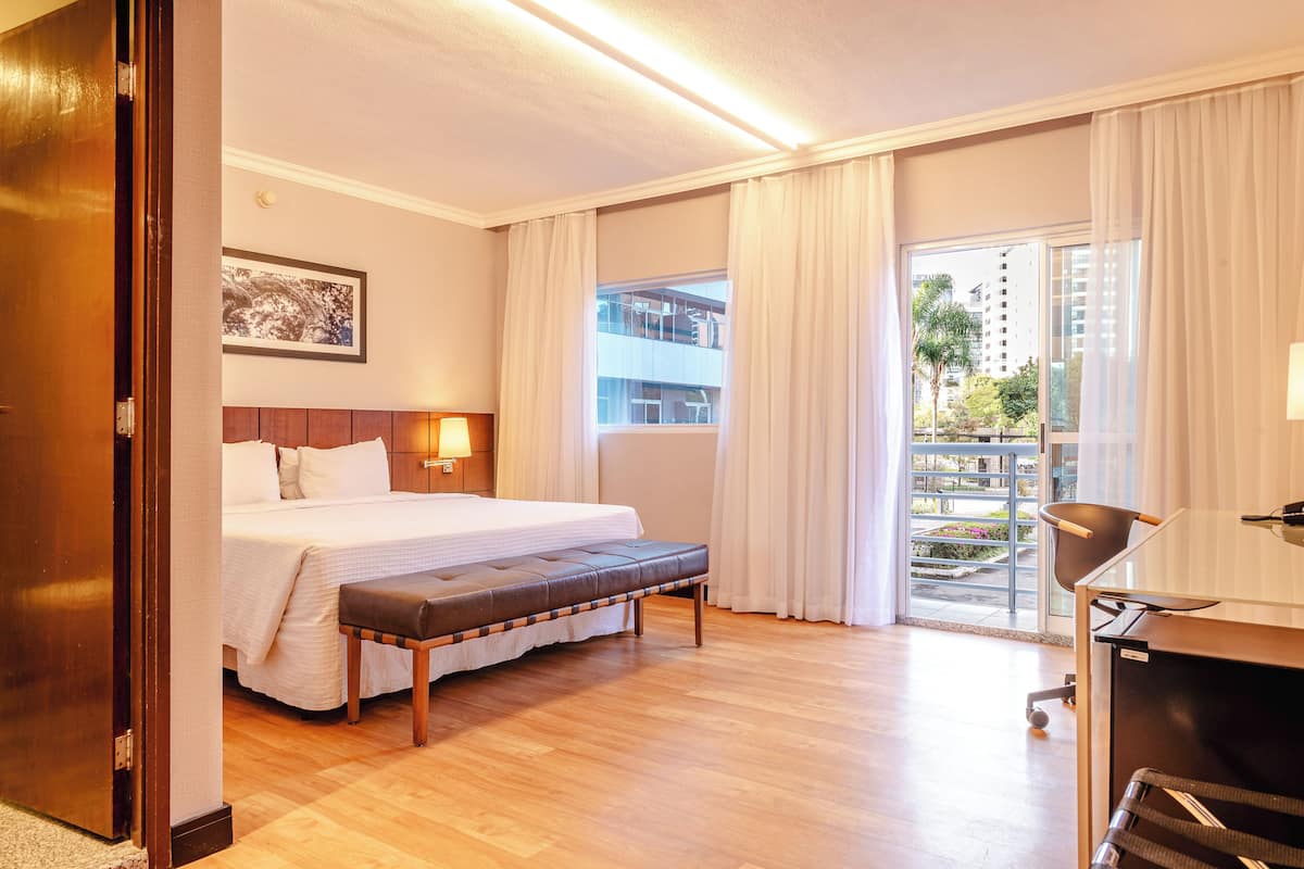 Une chambre d’hôtel avec un lit, un banc, un bureau et une vue sur l’extérieur.