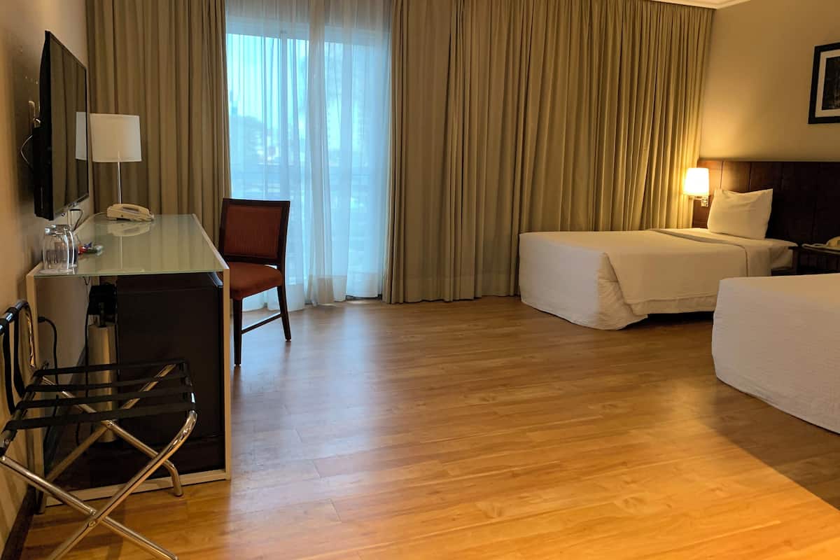 Une chambre d’hôtel équipée d’un bureau, de deux lits, d’une chaise et d’une grande fenêtre avec des rideaux.