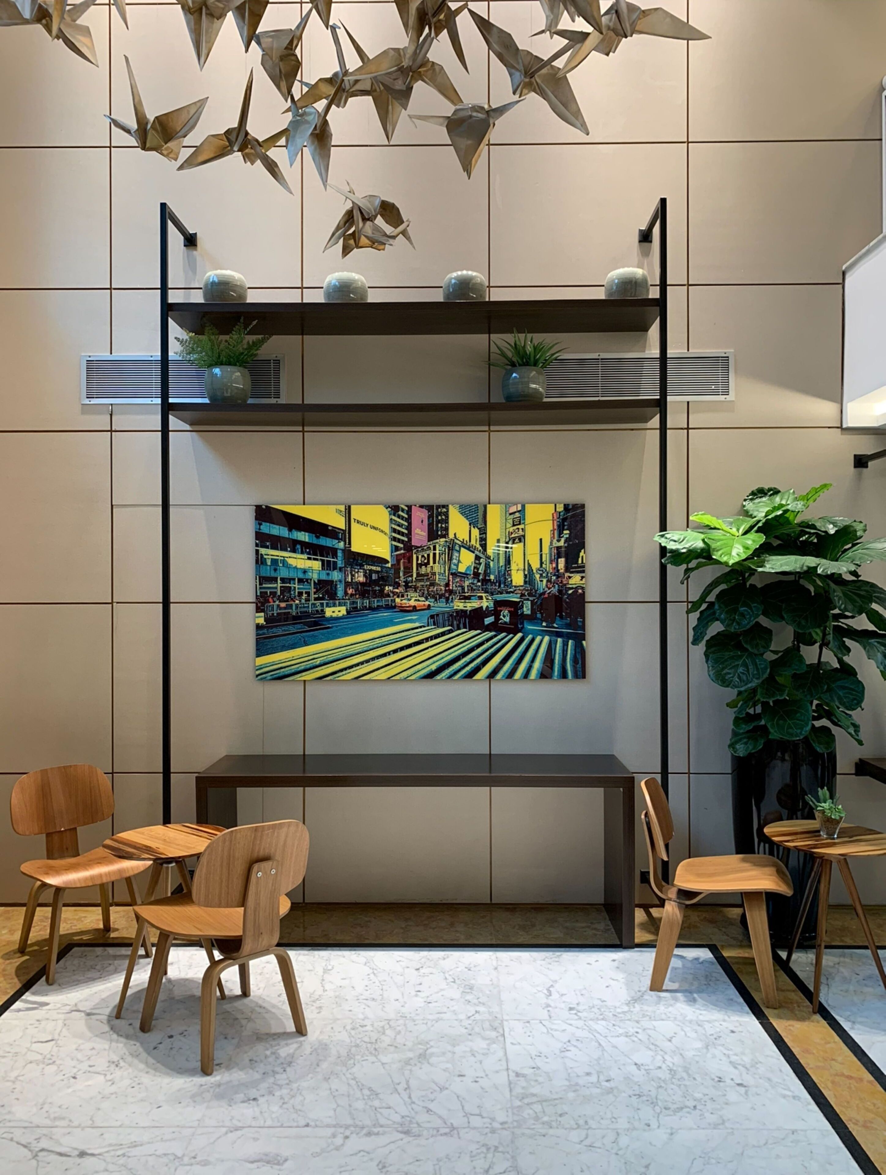 Un interior moderno con un banco, sillas de madera, un cuadro grande de un paisaje urbano y elementos decorativos colgantes.