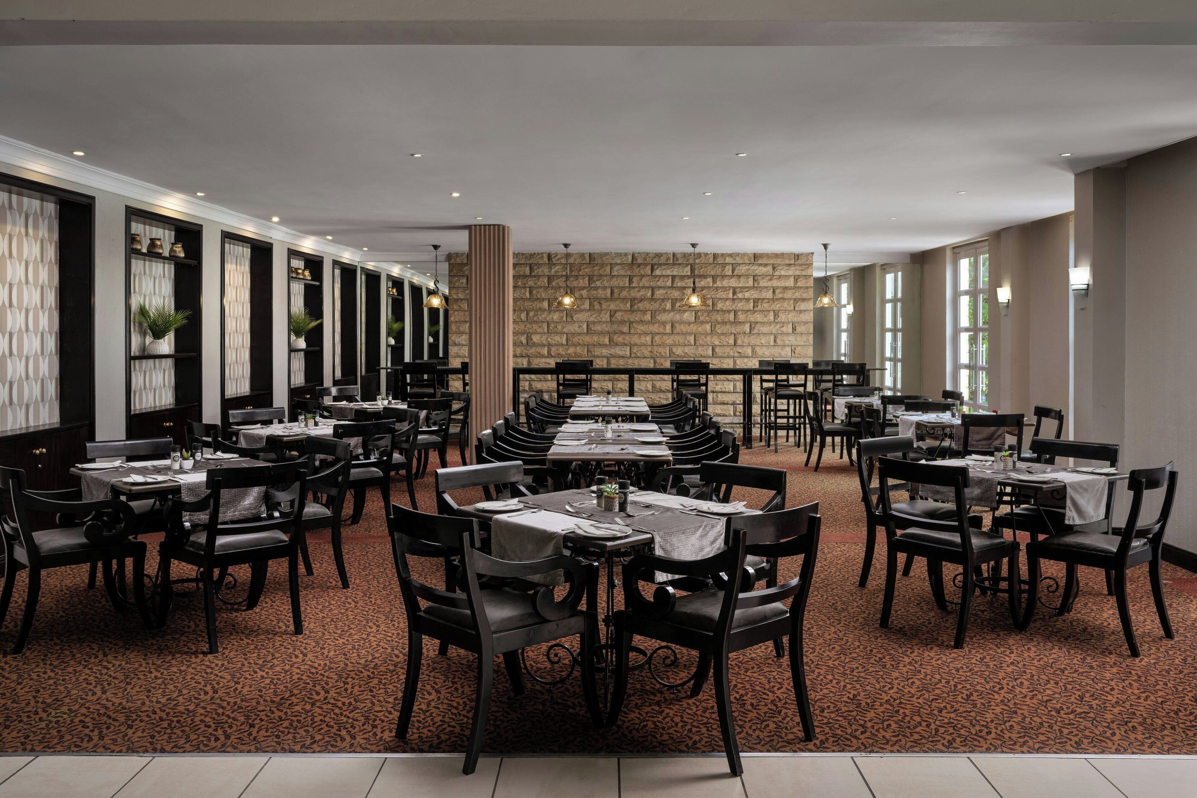 A spacious restaurant with multiple dining tables and chairs, a patterned carpet, and a stone wall in the background.