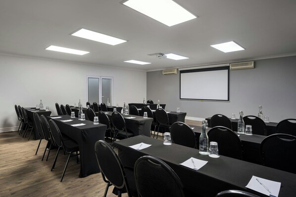 A conference room with multiple tables, chairs, and a projector screen.