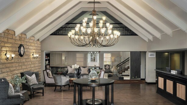 Un vaste espace de vie de style loft, doté d’un haut plafond, de murs en briques apparentes et d’un grand lustre. On y trouve un coin salon avec des canapés et des fauteuils, une table basse ronde et un comptoir d’accueil.