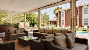 Un espace de détente extérieur abrité, aménagé avec des meubles en osier et une table basse en verre.