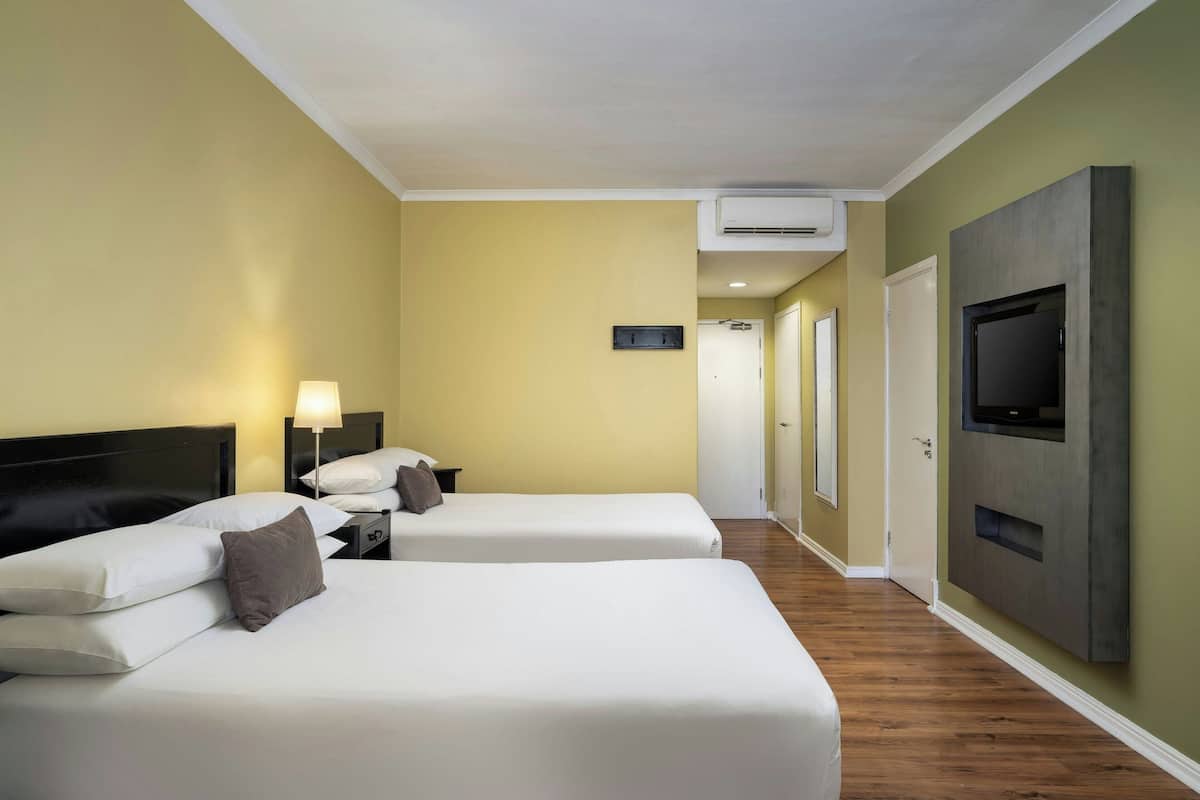 A hotel room with two beds, a TV mounted on the wall, and a hallway leading to another room.