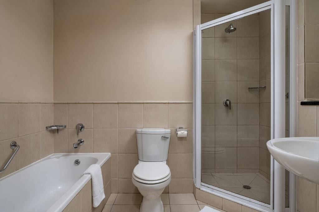Un baño con bañera, inodoro y ducha con mampara de vidrio.