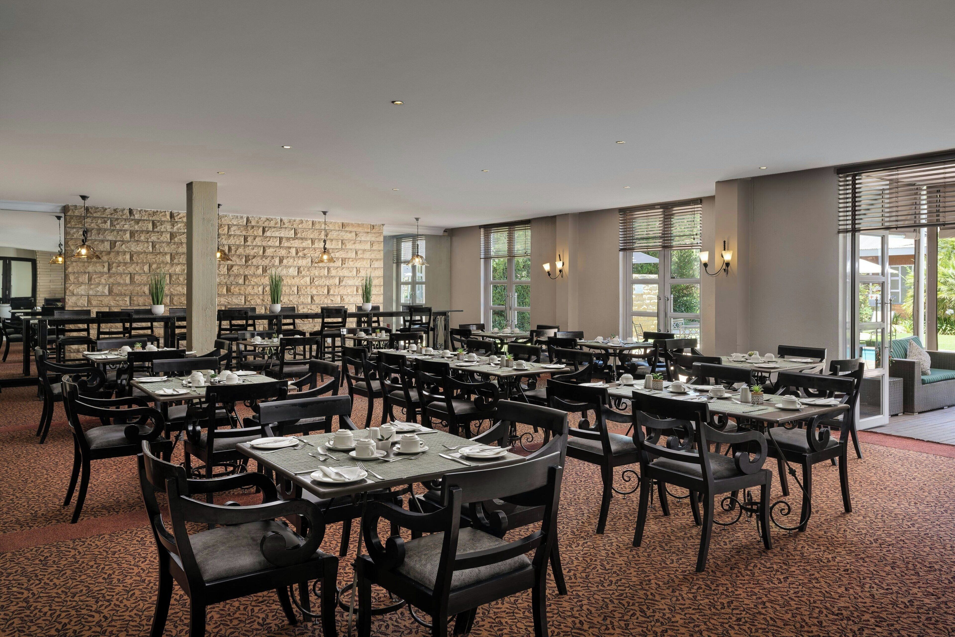 A spacious dining area with multiple tables and chairs, stone wall accents, and large windows providing natural light.