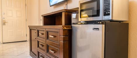 A kitchenette with a microwave, refrigerator, and a television mounted on the wall.