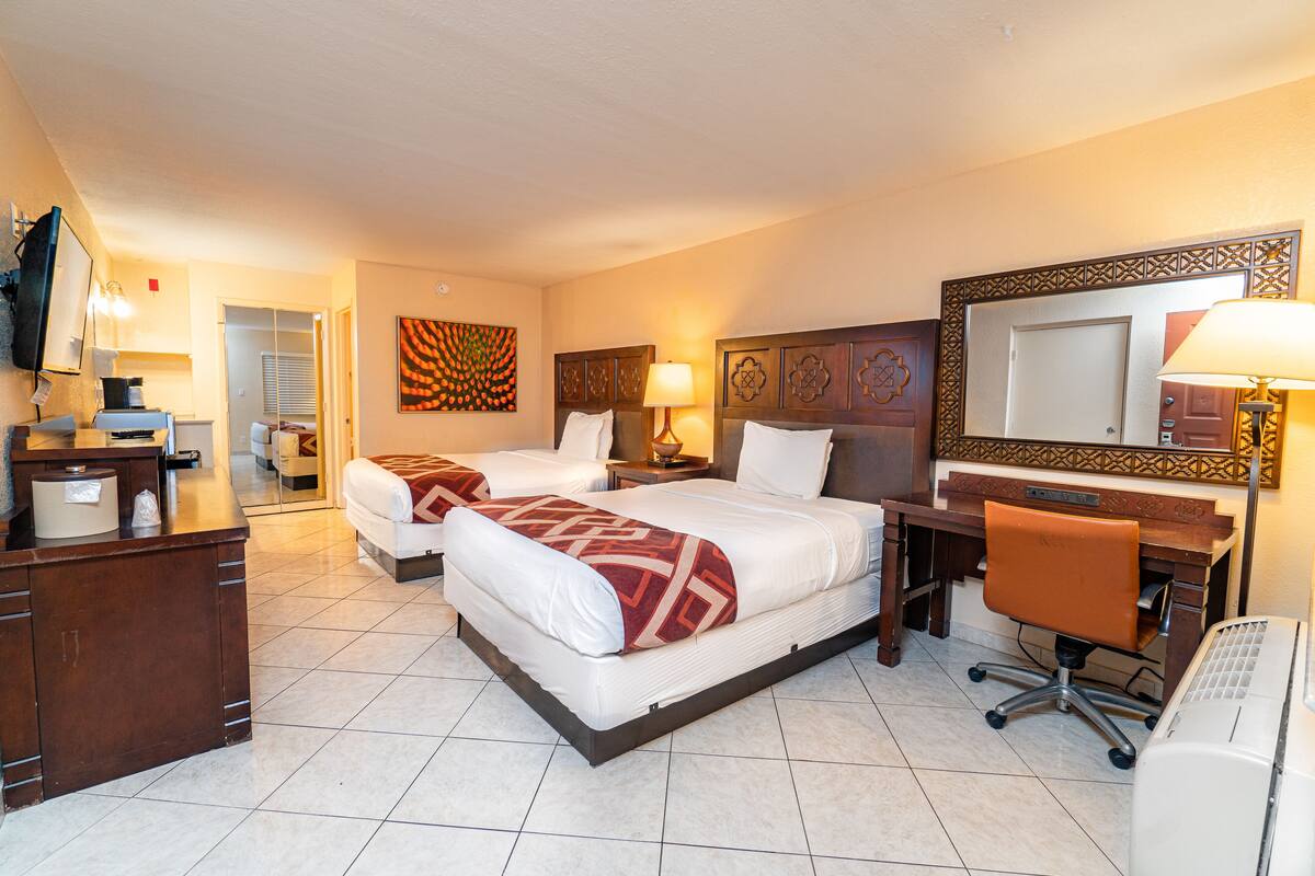 A hotel room with two beds, a desk, a chair, a TV, and a bathroom visible through an open door.