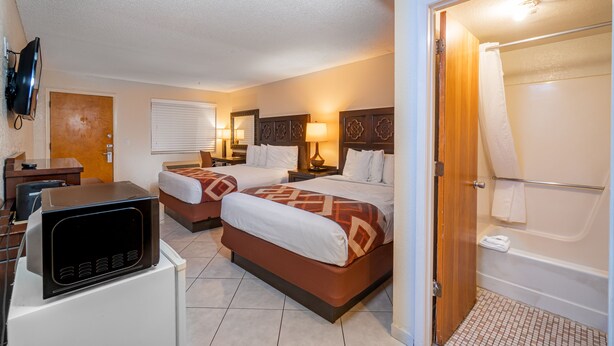 A hotel room with two beds, a TV, a desk, a bathroom with a bathtub, and a door. - Sevilla Inn - Near Medieval Times (Kissimmee)