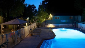 Une piscine à bord incurvé, entourée d’une terrasse avec des chaises longues et un espace salon abrité.
