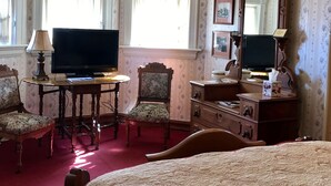 A hotel room with a bed, a television, a desk with a lamp, a chair, a dresser, and a mirror.