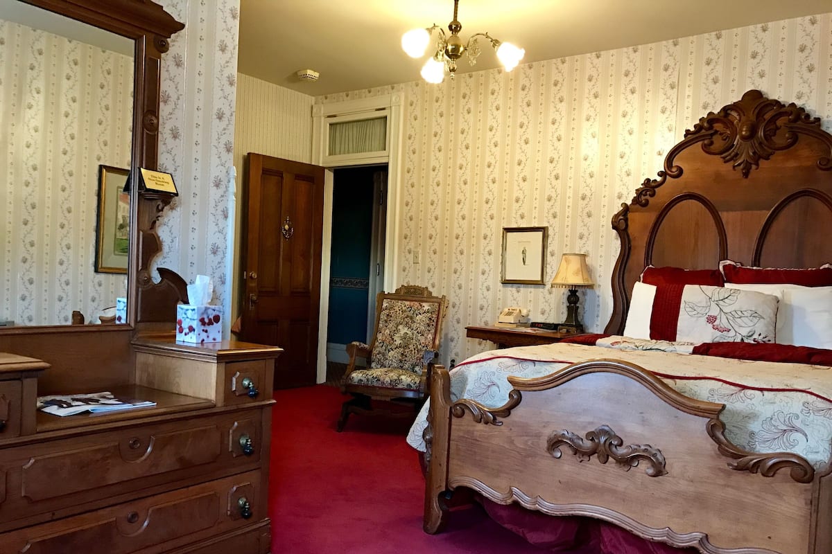 A bedroom with a wooden bed, a dresser, a chair, and a nightstand with a lamp.