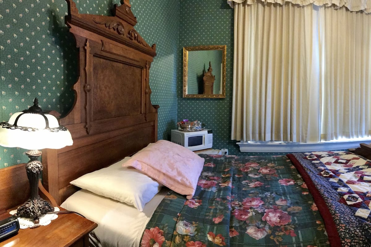 A room with a bed, a chair, a television, a dresser, and a mirror.