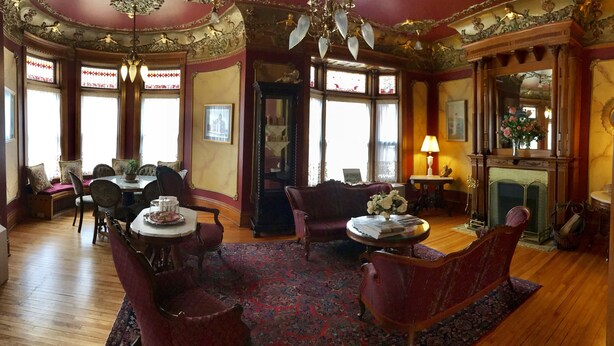 A room with a wooden floor, a fireplace, a chandelier, and a dining area with a table and chairs.