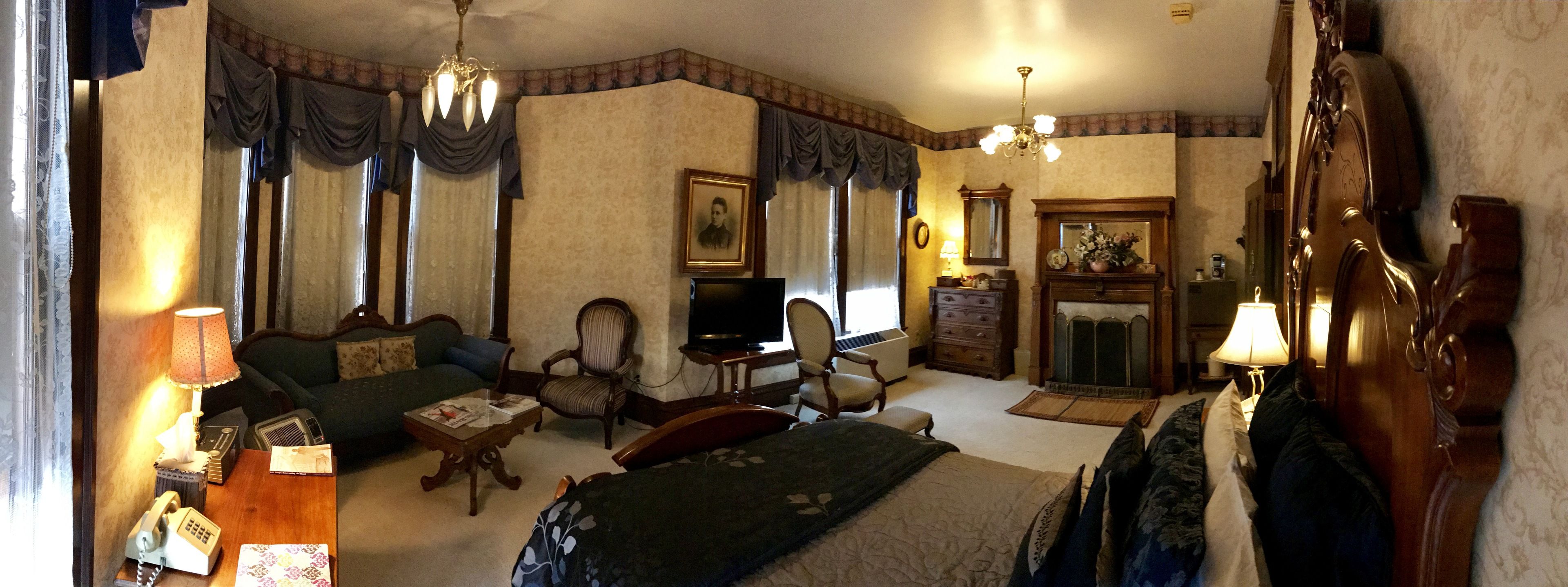 Une chambre d’hôtel traditionnelle avec un canapé, des fauteuils, une télévision, une cheminée et un lustre.