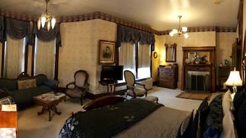 Une chambre d’hôtel traditionnelle avec un canapé, des fauteuils, une télévision, une cheminée et un lustre.
