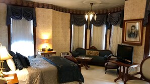 A hotel room with a bed, a sofa, a television, a desk with a lamp, and a chair.