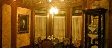 Una habitación con paneles de madera decorados, una araña, una mesa de comedor con sillas y un aparador con cristalería.