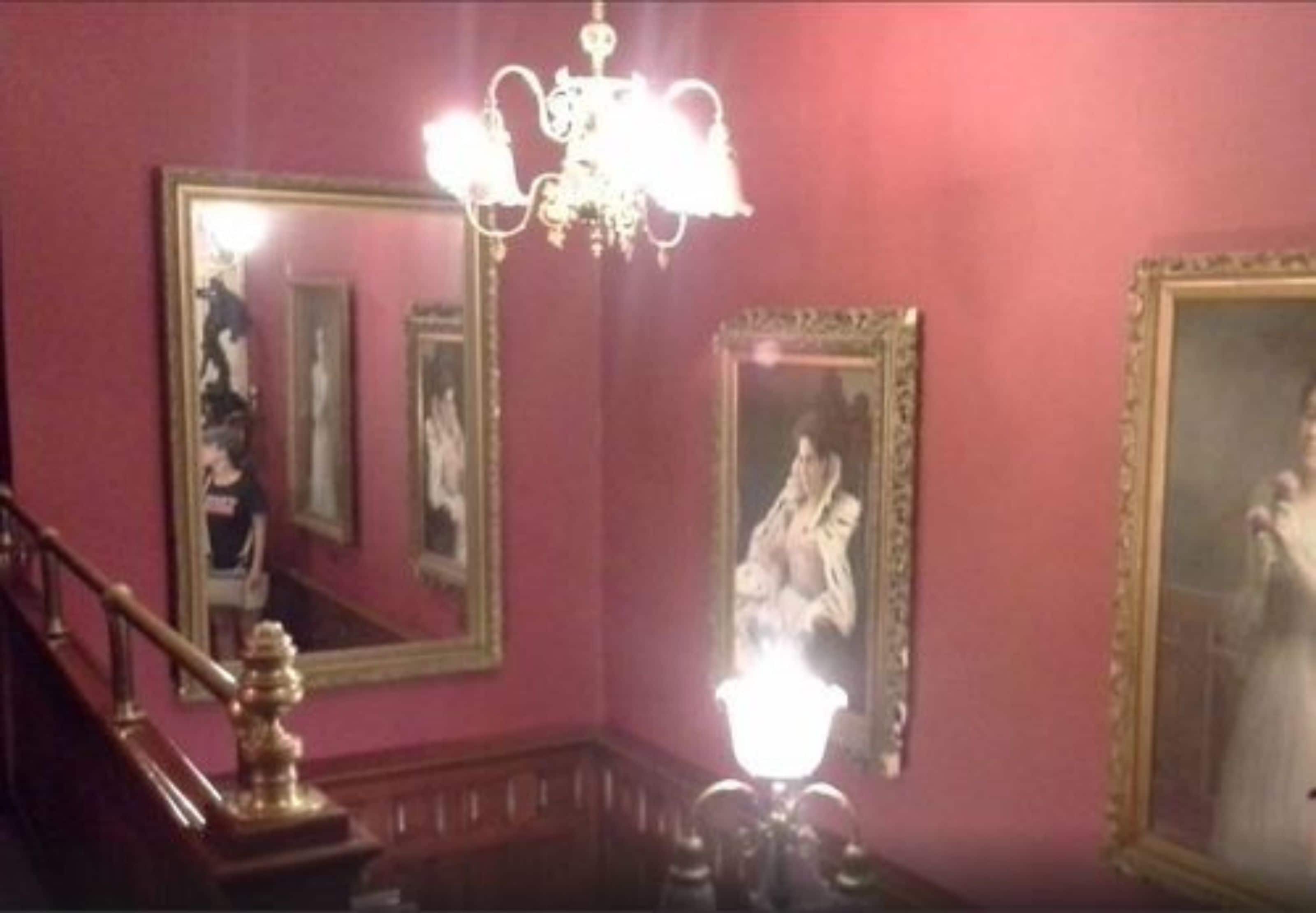 Ein Zimmer mit Treppe, einer Kristalllüster und mehreren gerahmten Spiegeln an den Wänden.