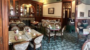 A traditional dining area with multiple tables and chairs, a coffee machine, and a cabinet with glass doors.