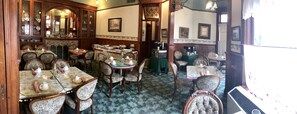 A traditional dining area with multiple tables and chairs, a coffee machine, and a cabinet with glass doors.