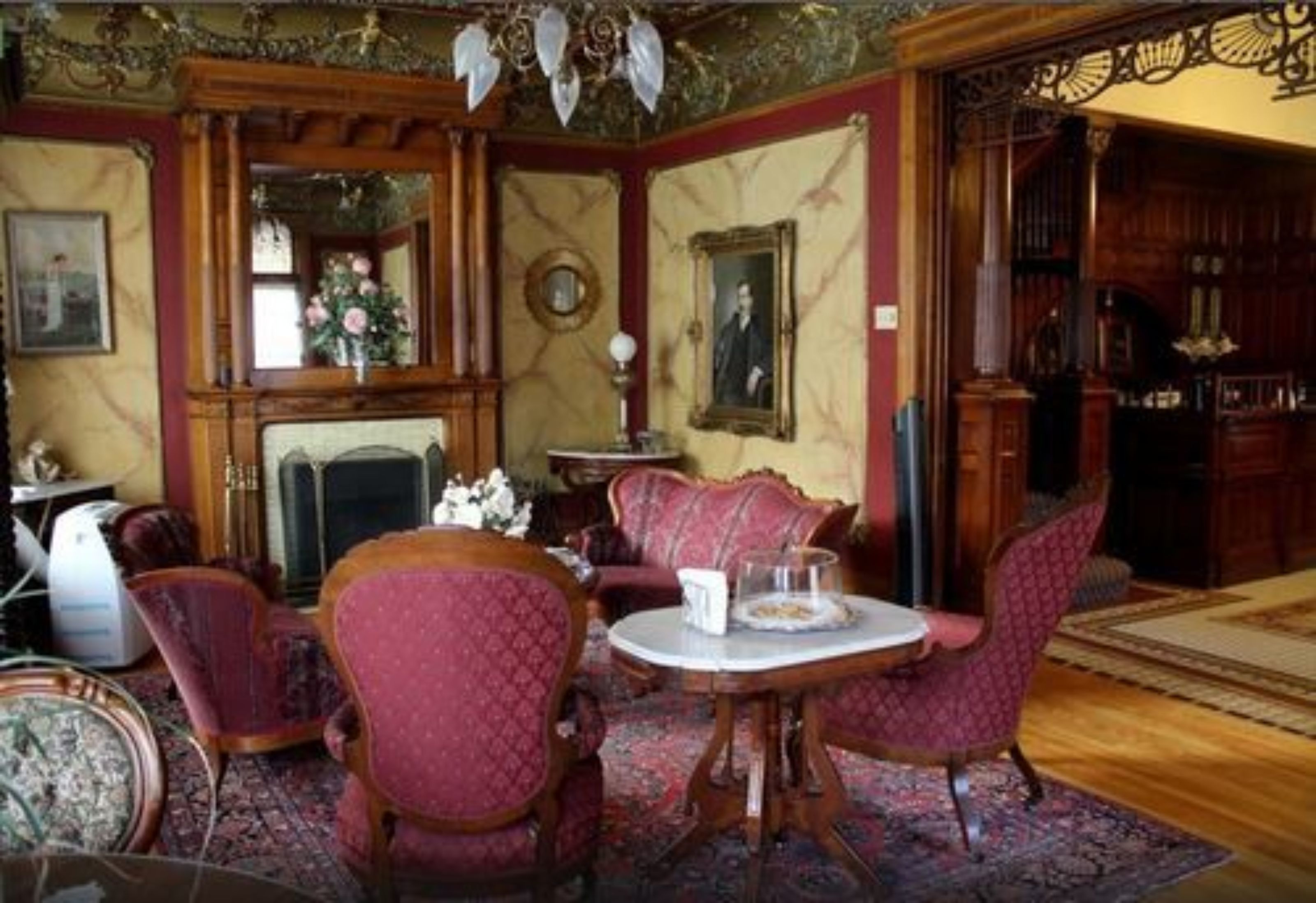 A room with a fireplace, red upholstered chairs, a round table, and a mirror.
