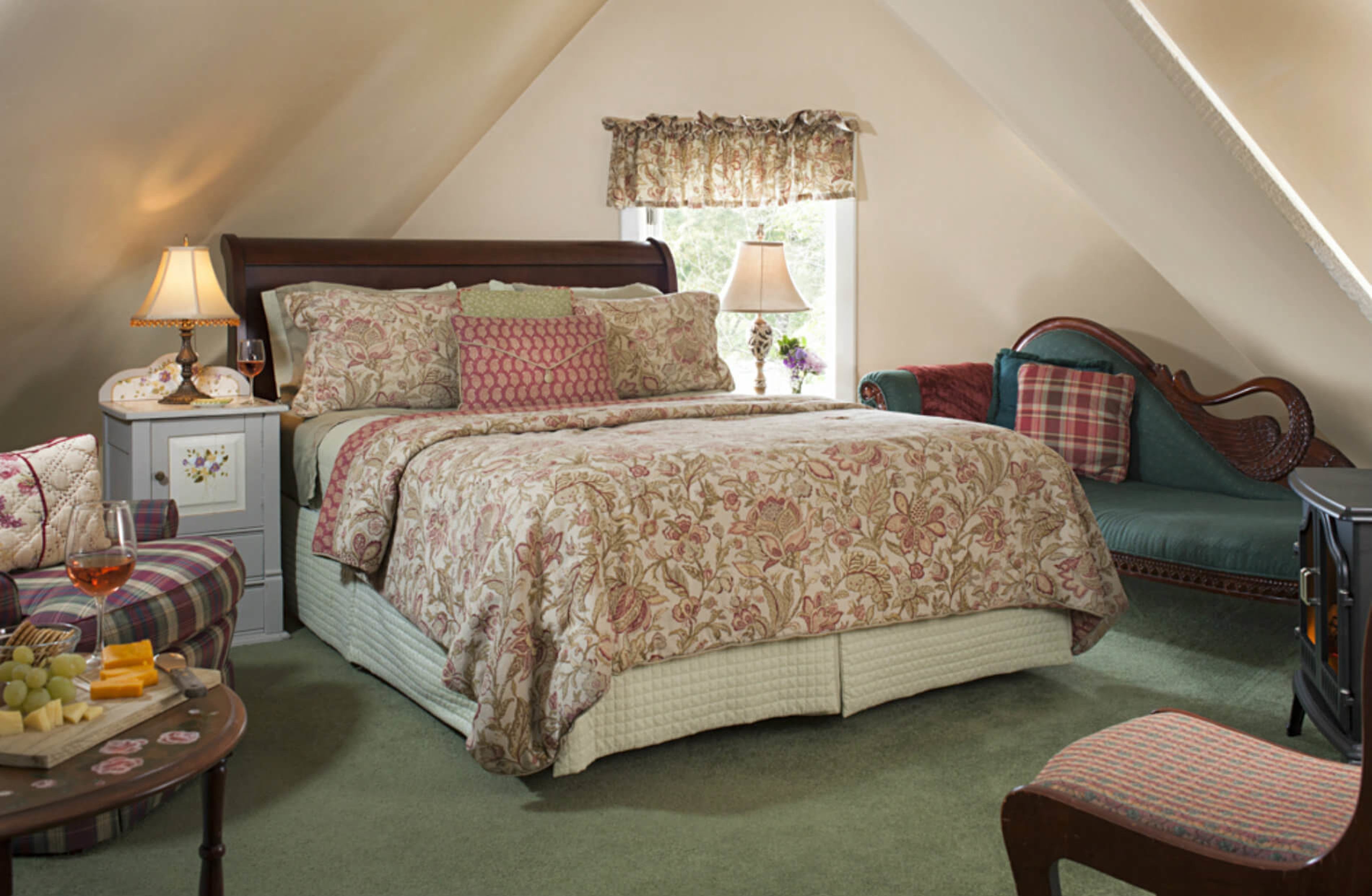 A cozy bedroom with a large bed, a nightstand with a lamp, a dresser, and a chair.