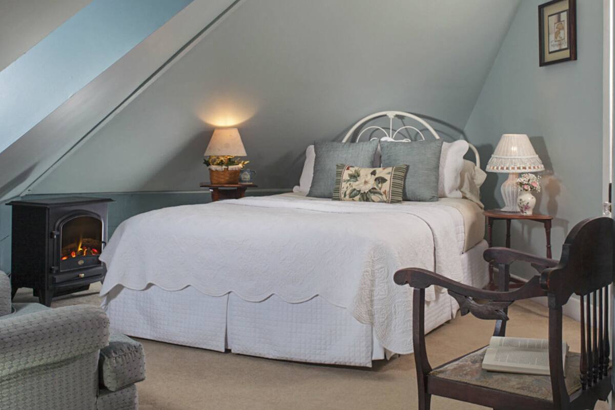 A cozy bedroom with a bed, a wooden chair, a small table, a lamp, and a fireplace.