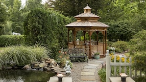 A gazebo in a garden with a pond, surrounded by greenery and a stone pathway. - Whistling Swan Inn (Stanhope)
