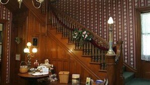 A wooden staircase with a floral arrangement at the top, a table with various items, and a patterned wallpaper. - Whistling Swan Inn (Stanhope)