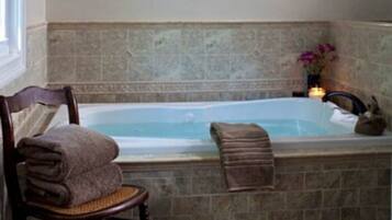A bathroom with a stone wall, a bathtub, a chair with a towel, and a small vase with flowers.