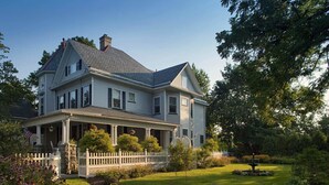 A two-story house with a porch, surrounded by a well-maintained garden and a white picket fence. - Whistling Swan Inn (Stanhope)