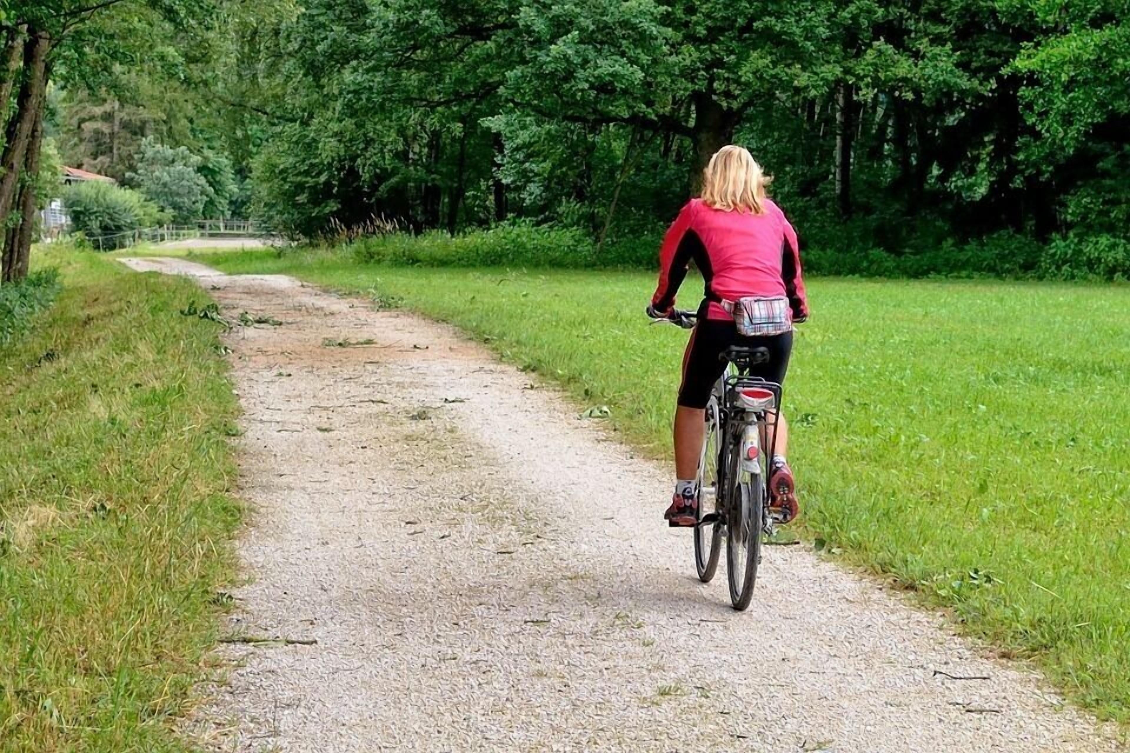 Une personne à vélo circule sur un chemin de gravier, entourée de verdure.