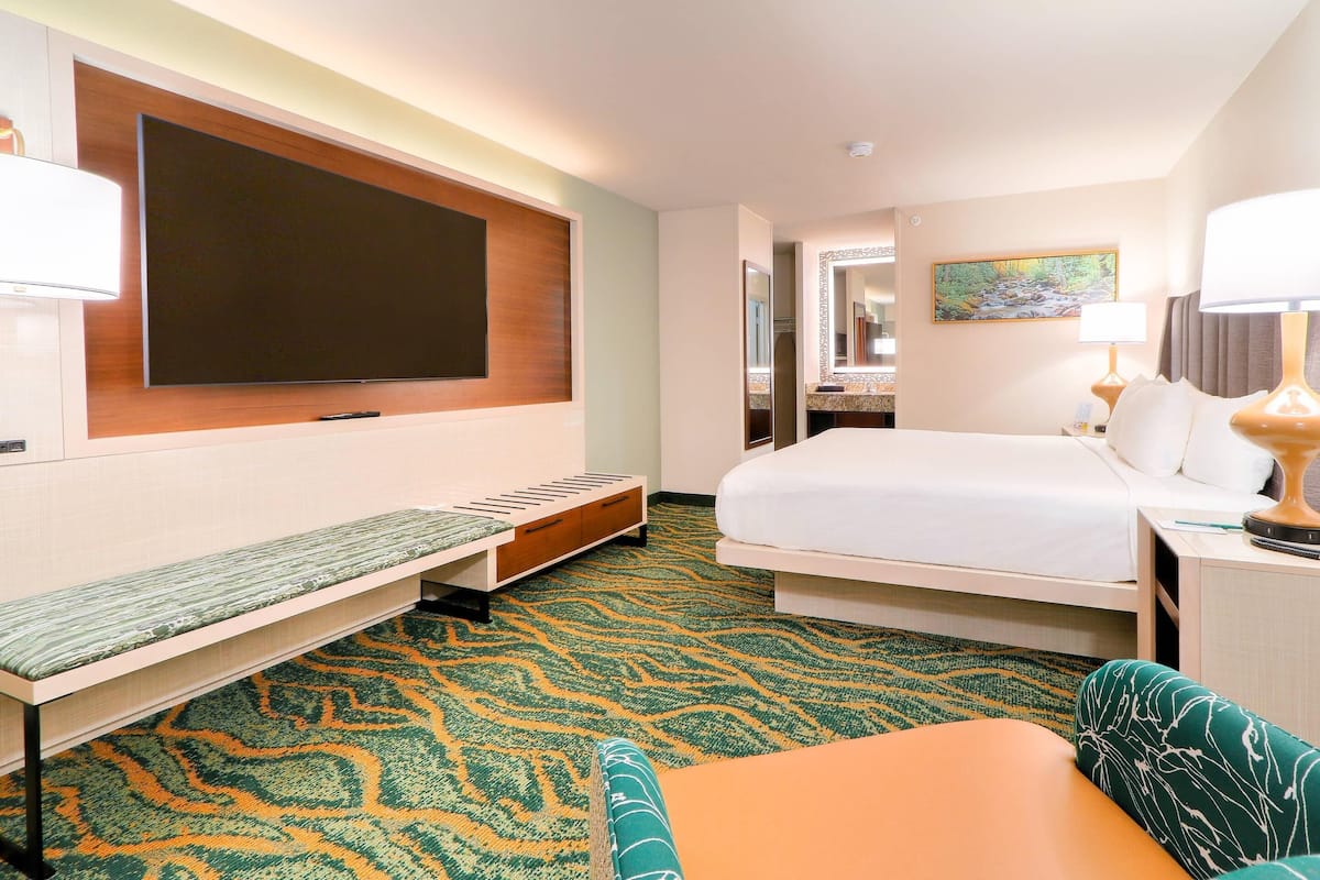 A hotel room with a bed, a bench, a TV, a lamp, and a patterned carpet.