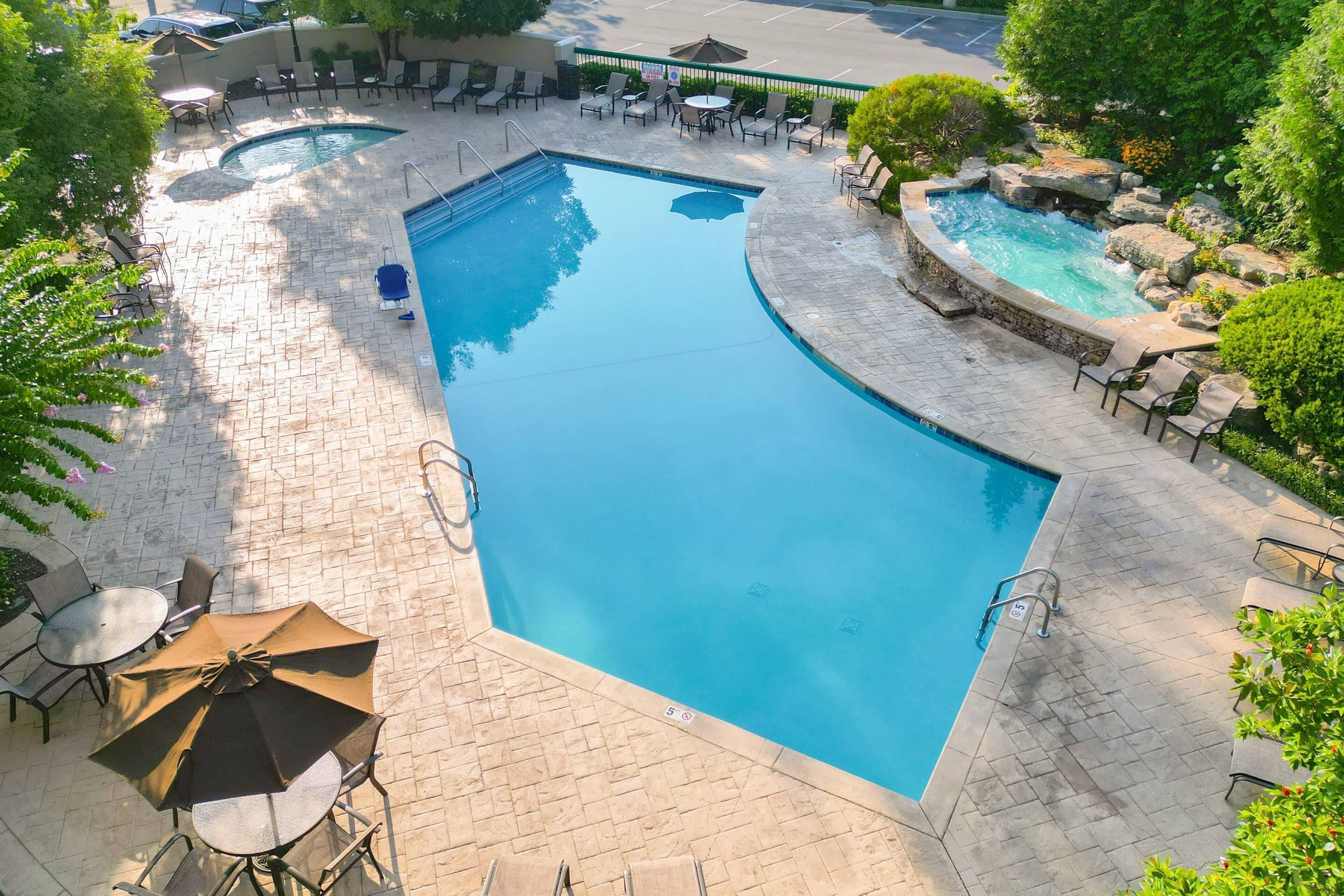 A swimming pool with a curved edge, surrounded by lounge chairs and a small waterfall feature.