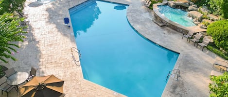 A swimming pool with a curved edge, surrounded by lounge chairs and a small waterfall feature.
