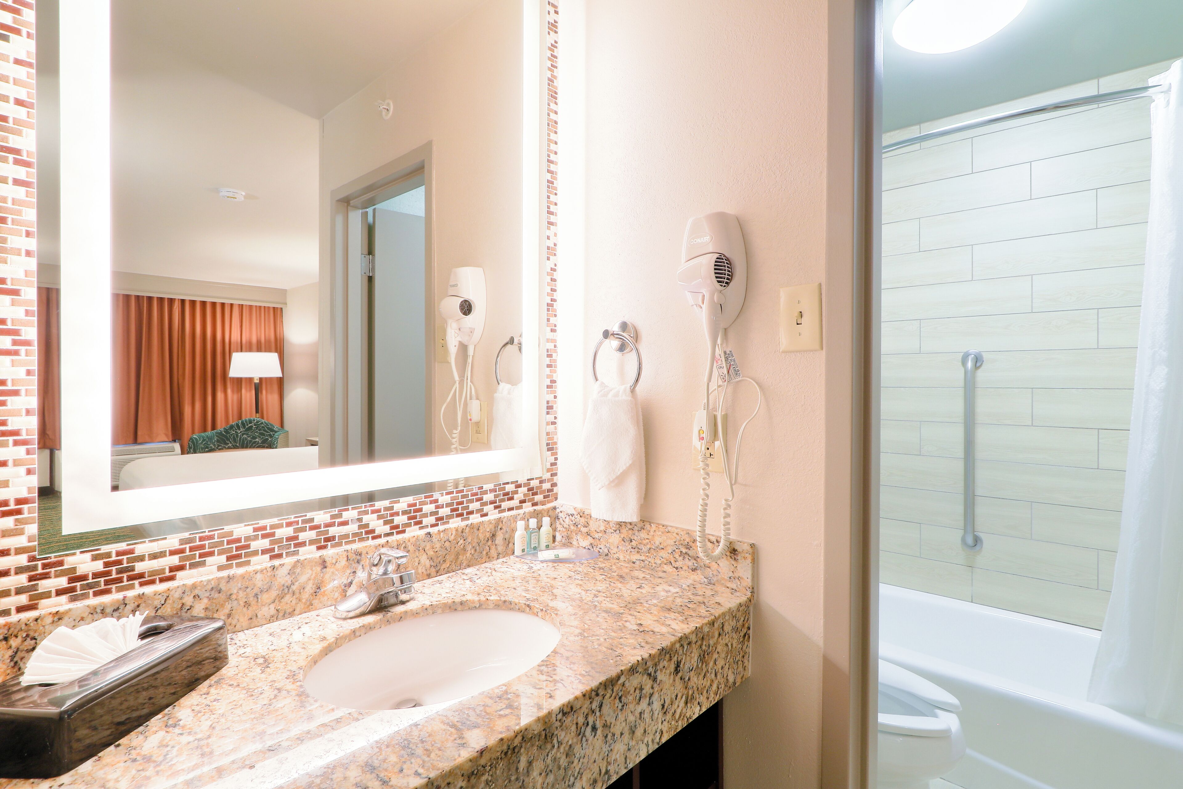 A bathroom with a granite sink, a mirror, a hairdryer, and a shower.