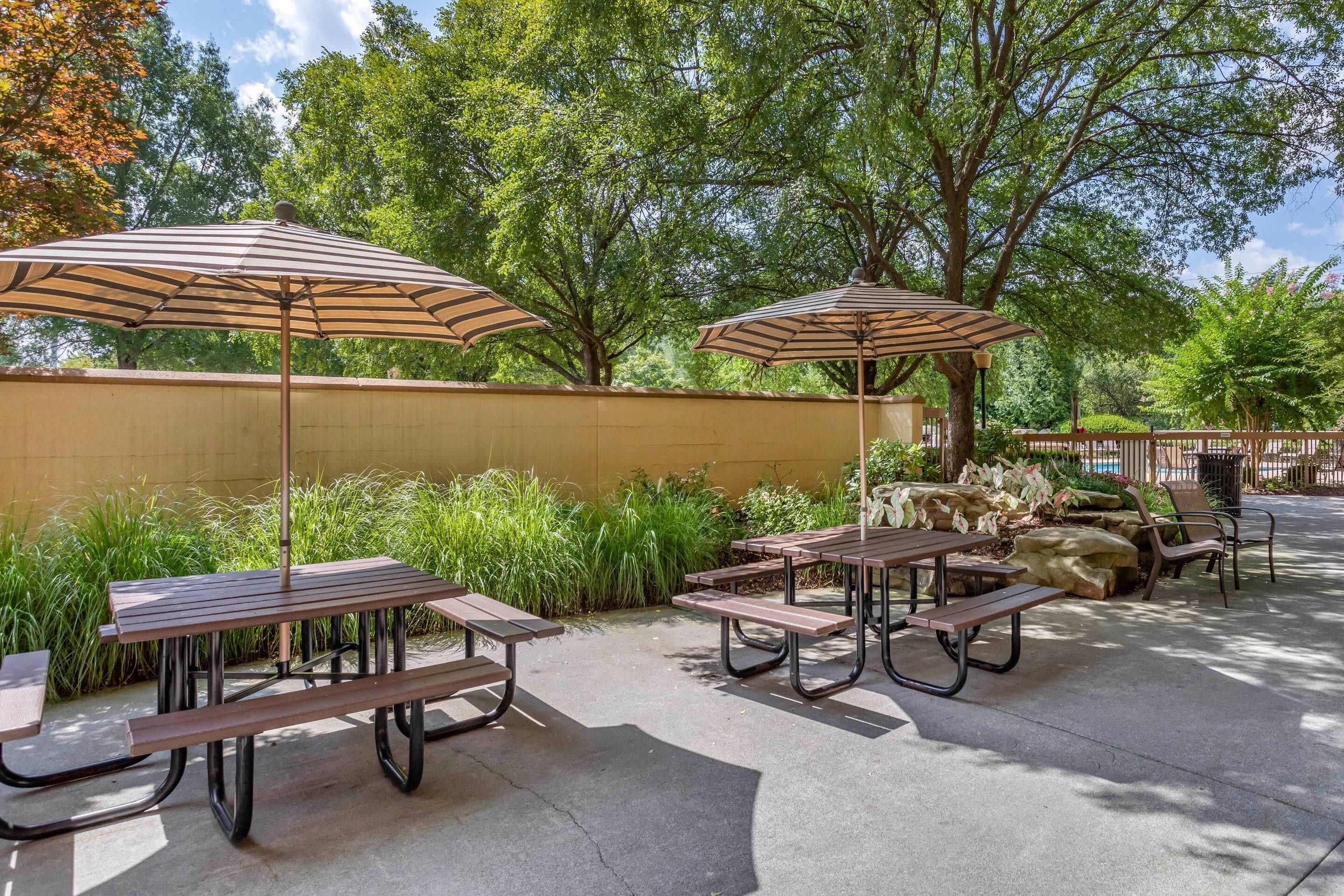 Un patio al aire libre con mesas de picnic y sombrillas a rayas.
