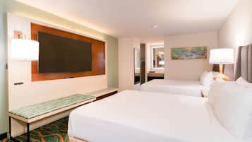 A hotel room with two beds, a bench, a TV, a mirror, and a painting on the wall.