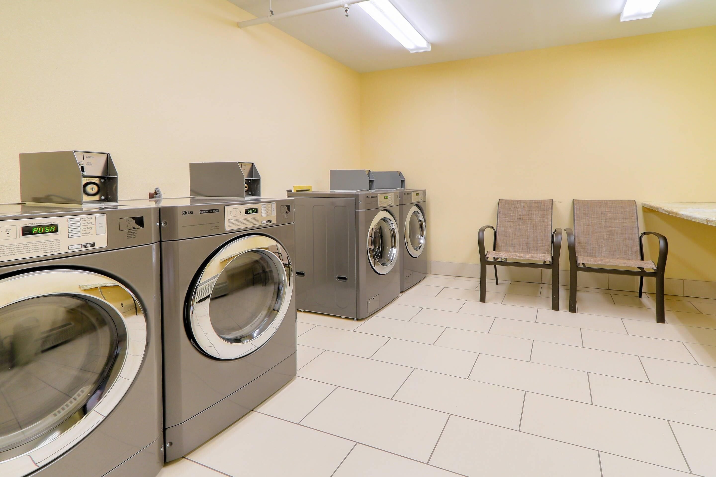 A laundry room with multiple washing machines, a dryer, and two chairs.