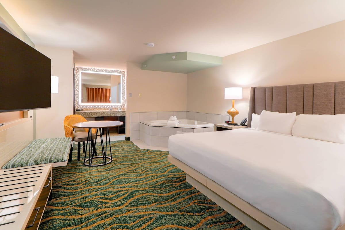 A hotel room with a bed, a desk, a chair, a TV, a mirror, and a bathroom.