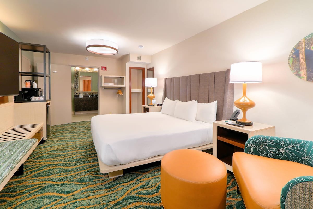 A hotel room with a bed, a desk with a lamp, a chair, and a small table.