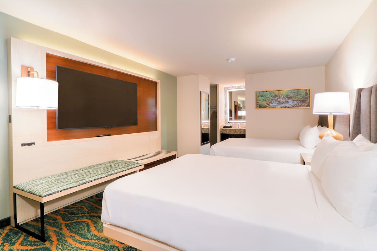 A hotel room with two beds, a bench, a TV, and a painting on the wall.